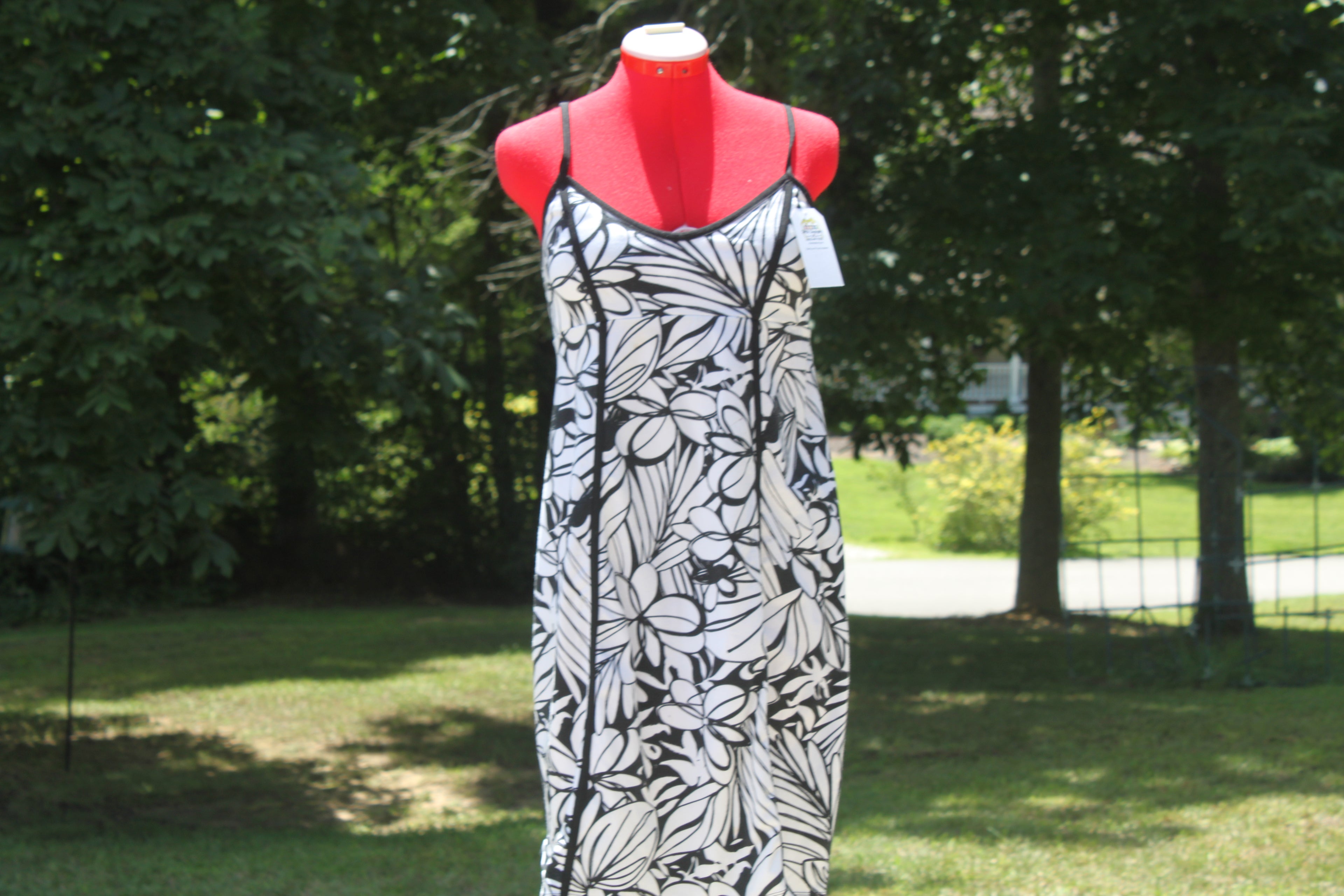 A sleeveless black and white floral print slip dress displayed on a red mannequin outdoors in a grassy yard with trees in the background.