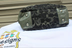 A Coach canvas and leather shoulder bag with the signature 'C' monogram pattern, olive green leather trim, and silver-tone snap buttons, resting on a white embroidered T-shirt.
